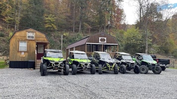 A gravel driveway with four green off-road vehicles parked in a row.