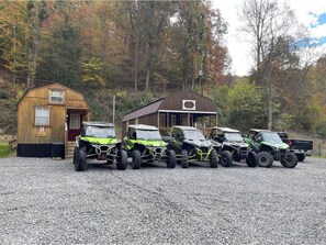 A gravel driveway with four green off-road vehicles parked in a row.