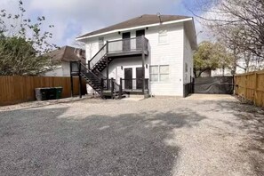 A two-story house with a front porch, a staircase leading to the second floor, and a fenced backyard. - East Downtown Loft + Full Kitchen (Houston)