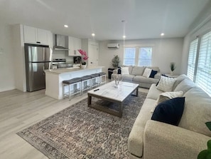 A modern living room with a sofa, coffee table, and a kitchen area with white cabinets and stainless steel appliances. - East Downtown Loft + Full Kitchen (Houston)