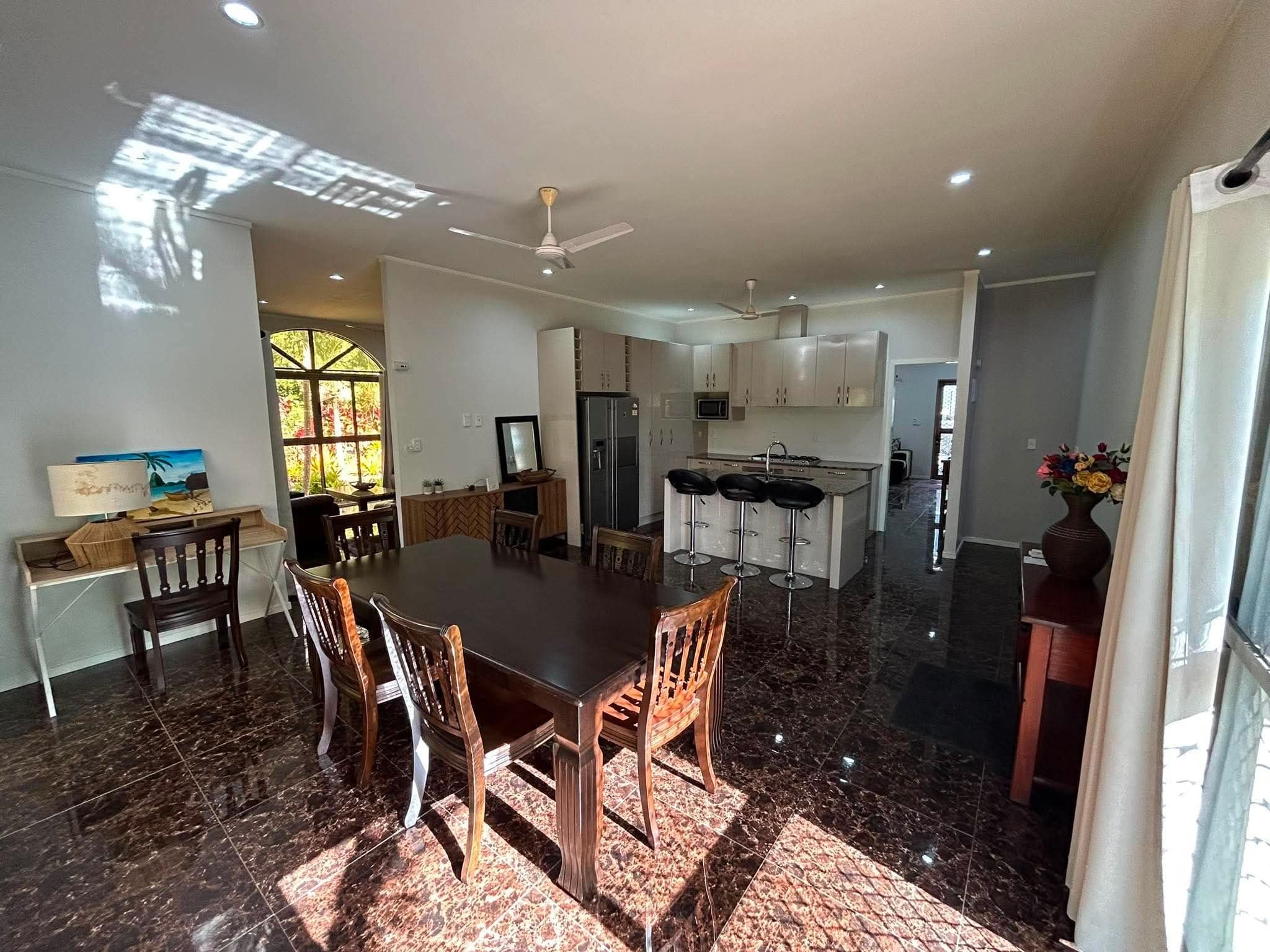 A spacious dining area with a large table and chairs, a kitchen with modern appliances, and a view through a window.