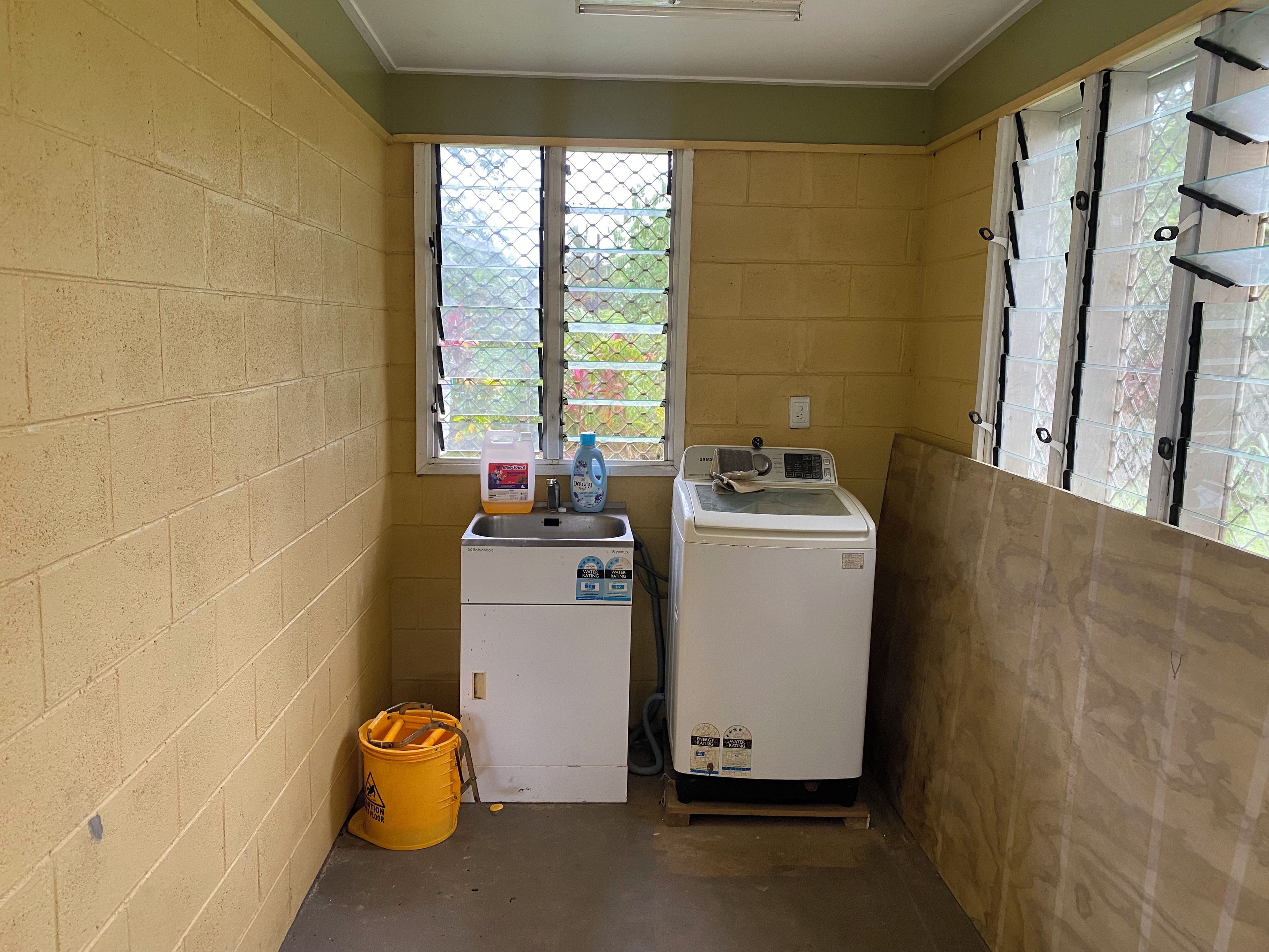 A small laundry room with a washing machine, a dryer, and a yellow bucket on the floor.