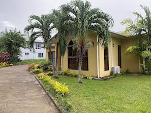 A building with a yellow exterior, surrounded by a well-maintained lawn and various tropical plants.