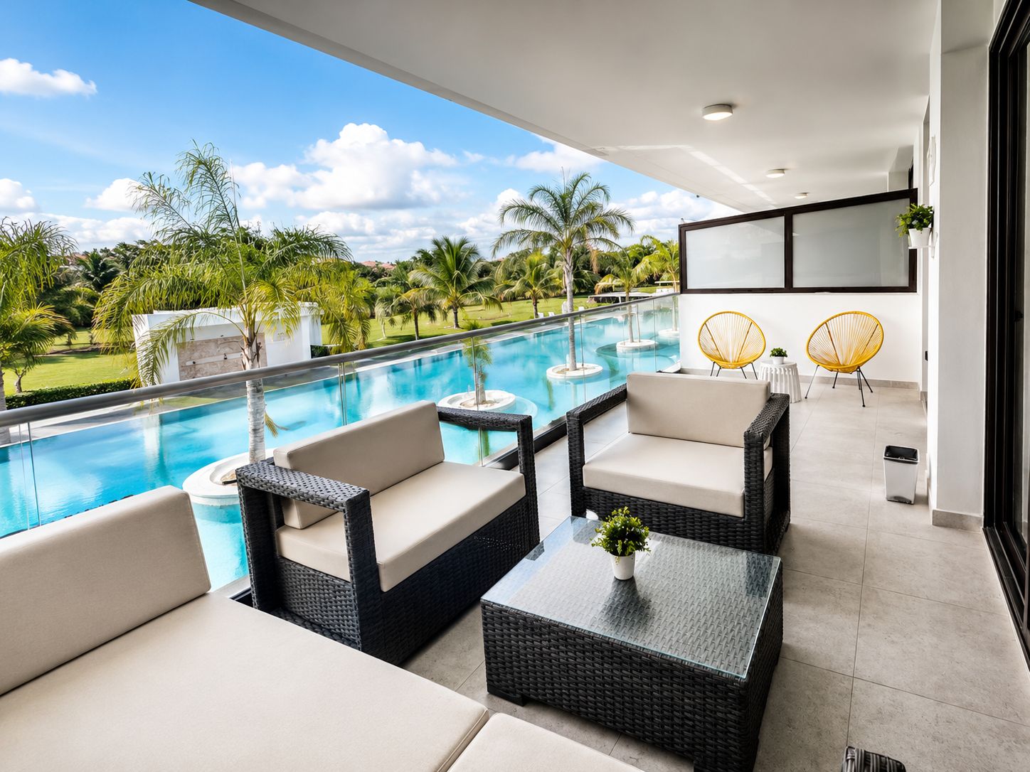 Uma área de estar moderna ao ar livre, com piscina, móveis de vime e vista para uma paisagem tropical.