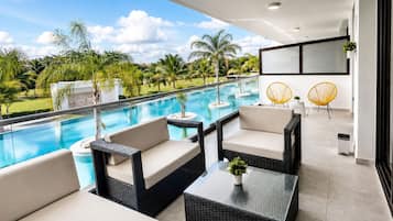 Uma área de estar moderna ao ar livre, com piscina, móveis de vime e vista para uma paisagem tropical.