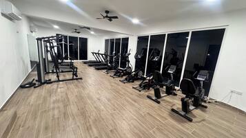 Een sportschool met diverse fitnessapparaten, grote ramen en plafondventilatoren.
