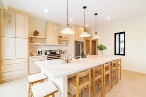 Een moderne keuken met een centraal eiland, hangende lampen en uitzicht op het buiten.