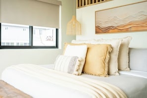 A bed with a white comforter and multiple pillows, a window with a view, and a wall-mounted lamp. - Sargassum-Free Luxury Beachfront Villa, Chef, Pool (San Pedro)