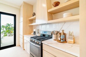 A modern kitchen with a gas stove, a coffee maker, and wooden shelves. - Sargassum-Free Luxury Beachfront Villa, Chef, Pool (San Pedro)