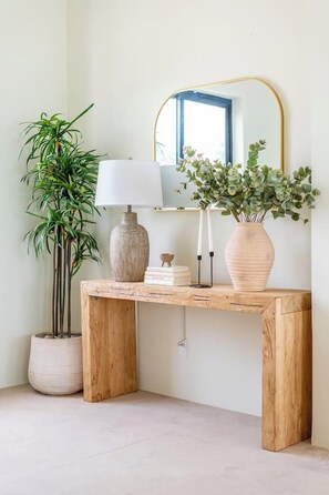 Een houten console tafel met een witte vaas, een lamp en een spiegel.