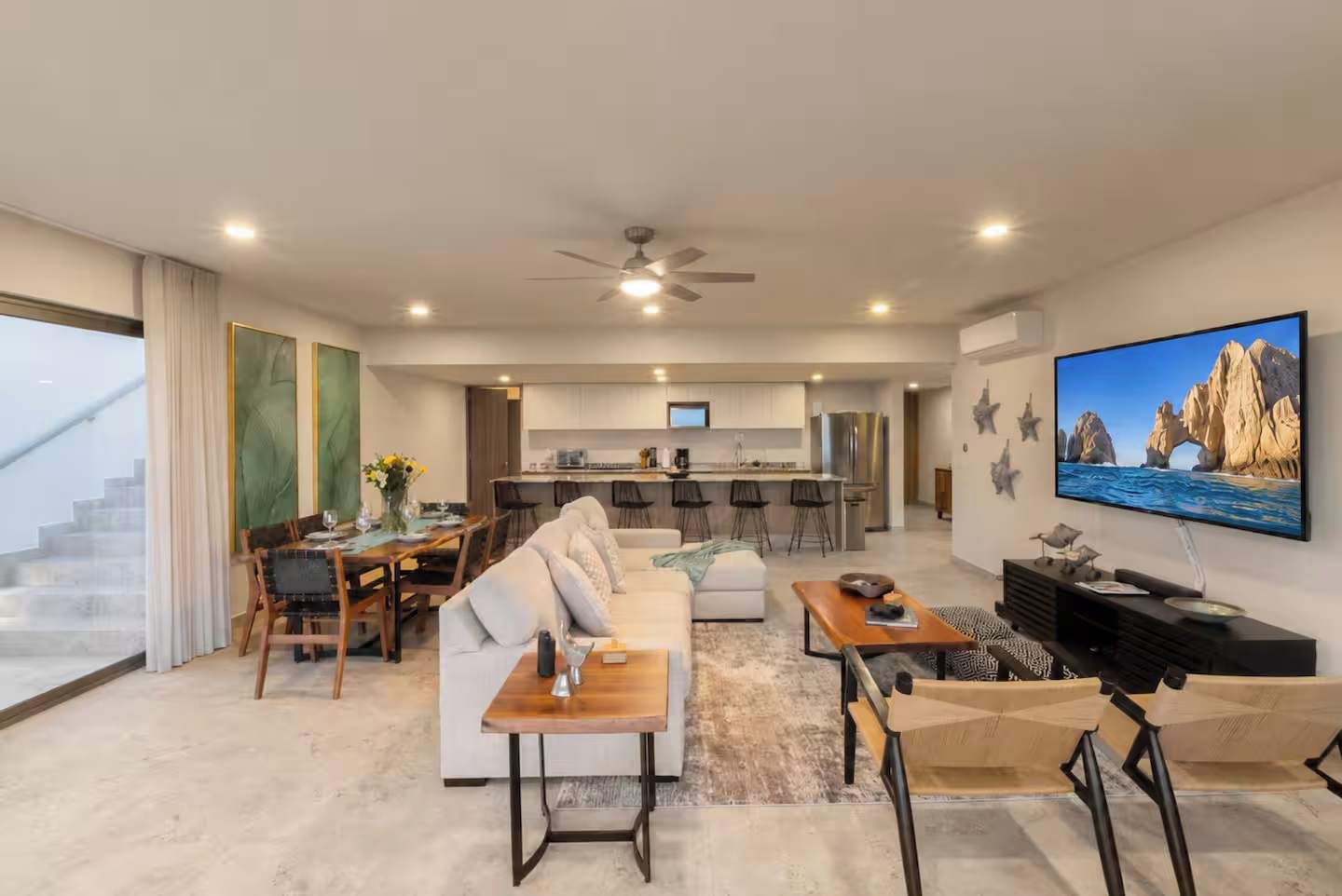 Un grand espace de vie comprenant un canapé, une table basse et un téléviseur. Au fond, on aperçoit une cuisine avec un coin repas.
