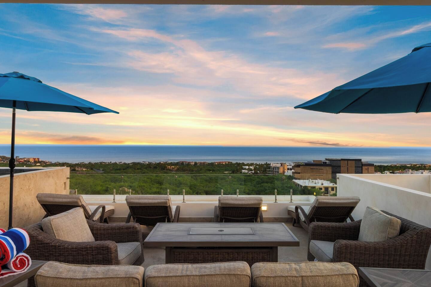 An outdoor seating area with wicker furniture and umbrellas, overlooking a coastal landscape.