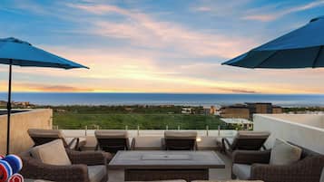 An outdoor seating area with wicker furniture and umbrellas, overlooking a coastal landscape.