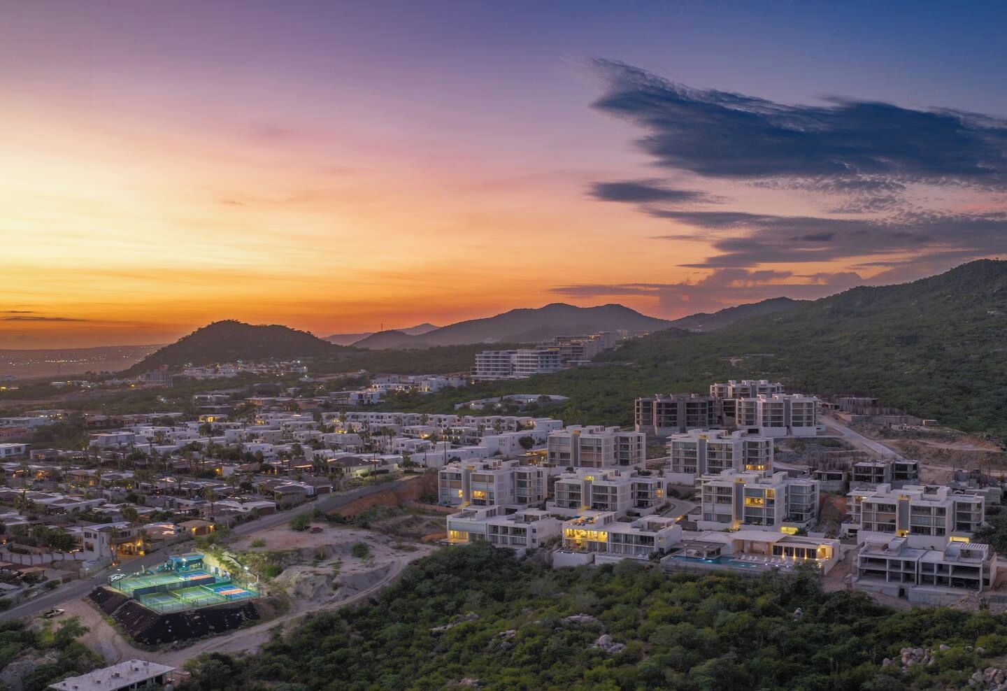 A residential area with modern buildings, a swimming pool, and a hilly landscape in the background.