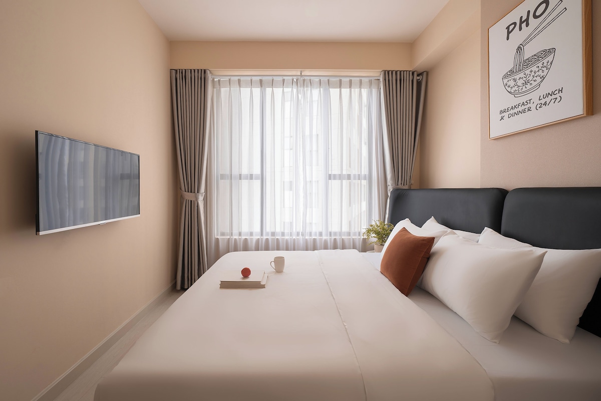 A hotel room with a bed, a TV, a window with curtains, and a wall-mounted sign.