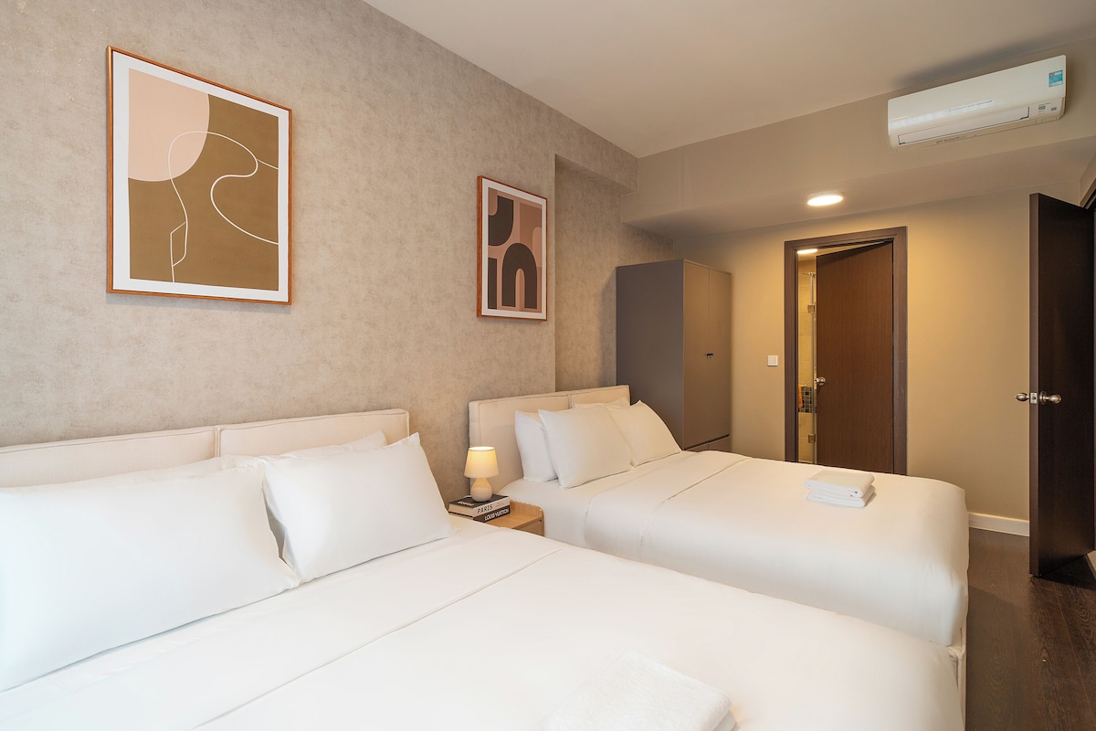 A hotel room with two beds, a nightstand with a lamp, and a door leading to a bathroom.