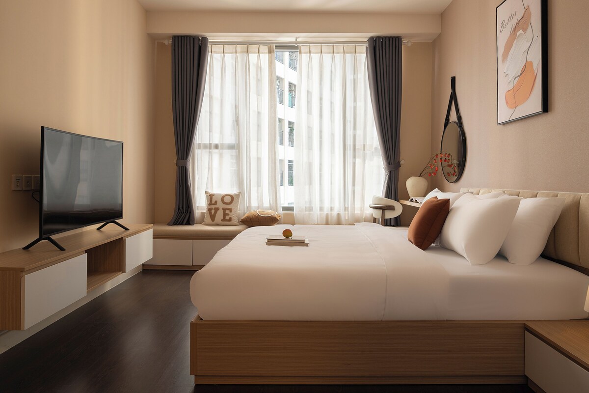 A hotel room with a large bed, a TV, a desk, and a window with curtains.