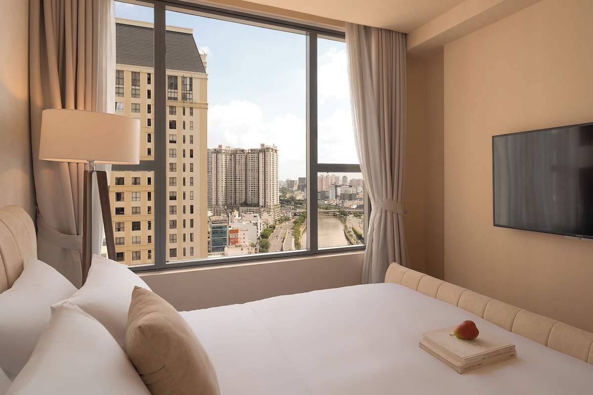 A hotel room with a large window, a bed, a flat-screen TV, and a book on the nightstand.