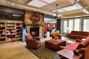 Eine Lobby mit Kamin, Sofas, einer Bücherwand und einem Empfangstresen.