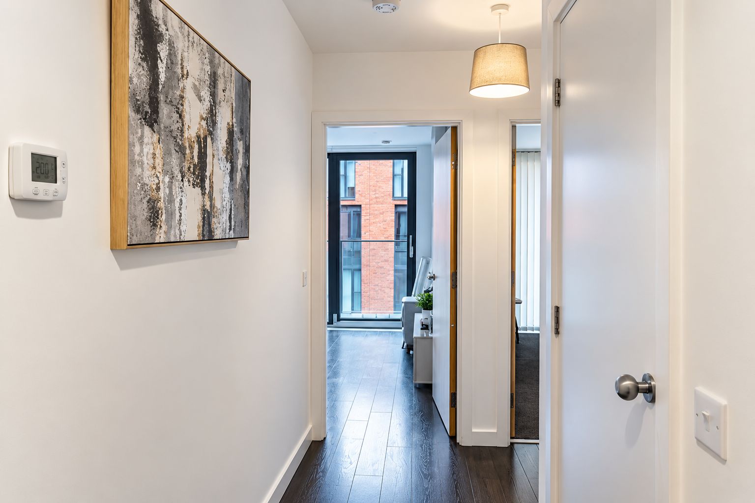 A hallway with a modern light fixture, a thermostat, and a large abstract painting on the wall.