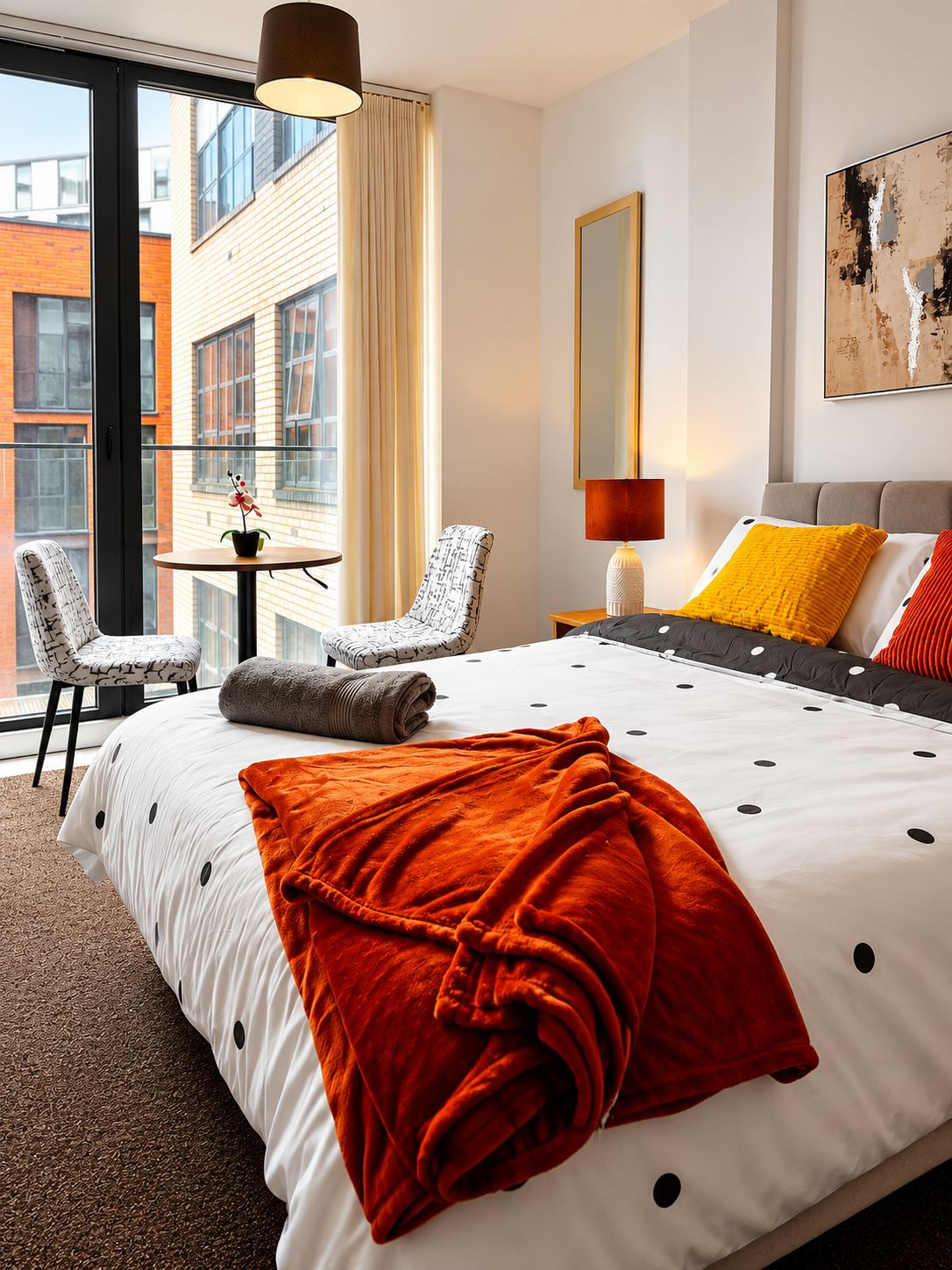 Habitación de hotel con una cama grande, un escritorio con silla, una ventana con cortinas, un cuadro en la pared y vistas a edificios.