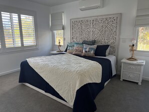 A bedroom with a large bed, a nightstand, a wall-mounted air conditioner, and a window with blinds. - Relaxing getaway with the family  on the water. (South Stradbroke)