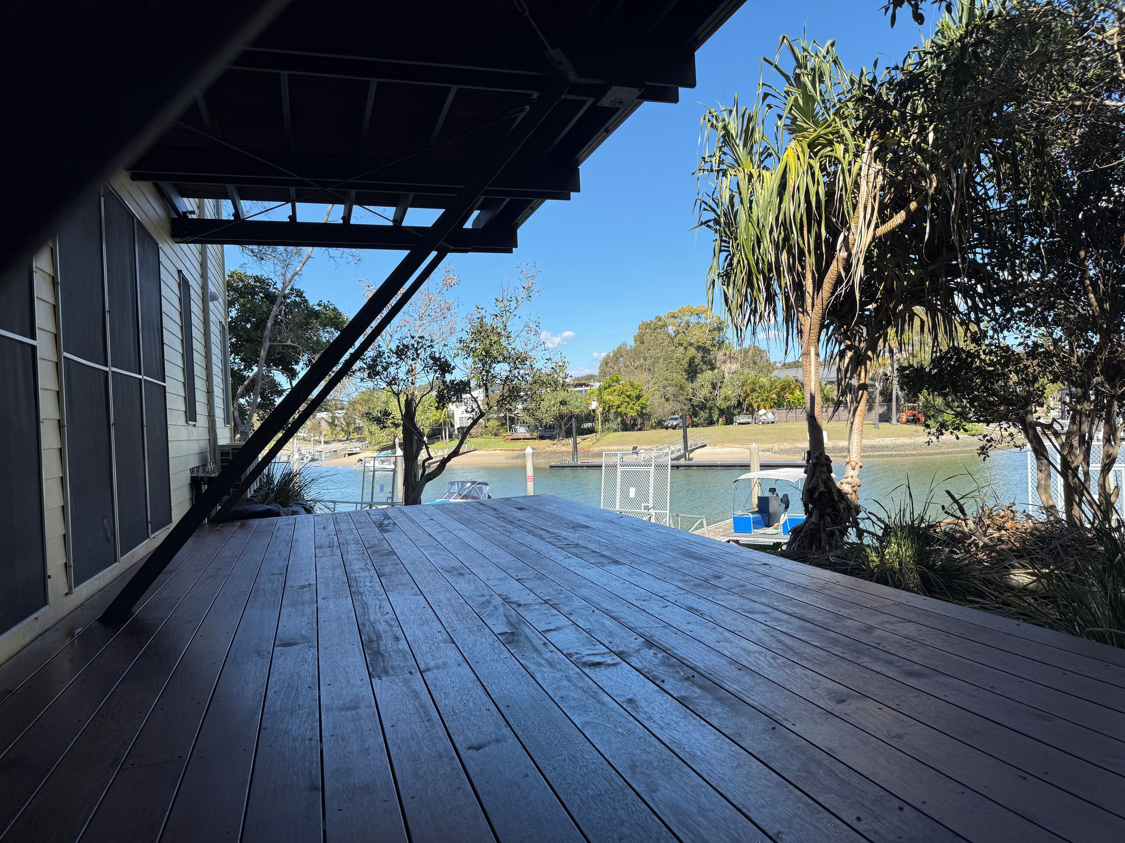 A wooden deck with a view of a calm lake, surrounded by trees and a clear sky.