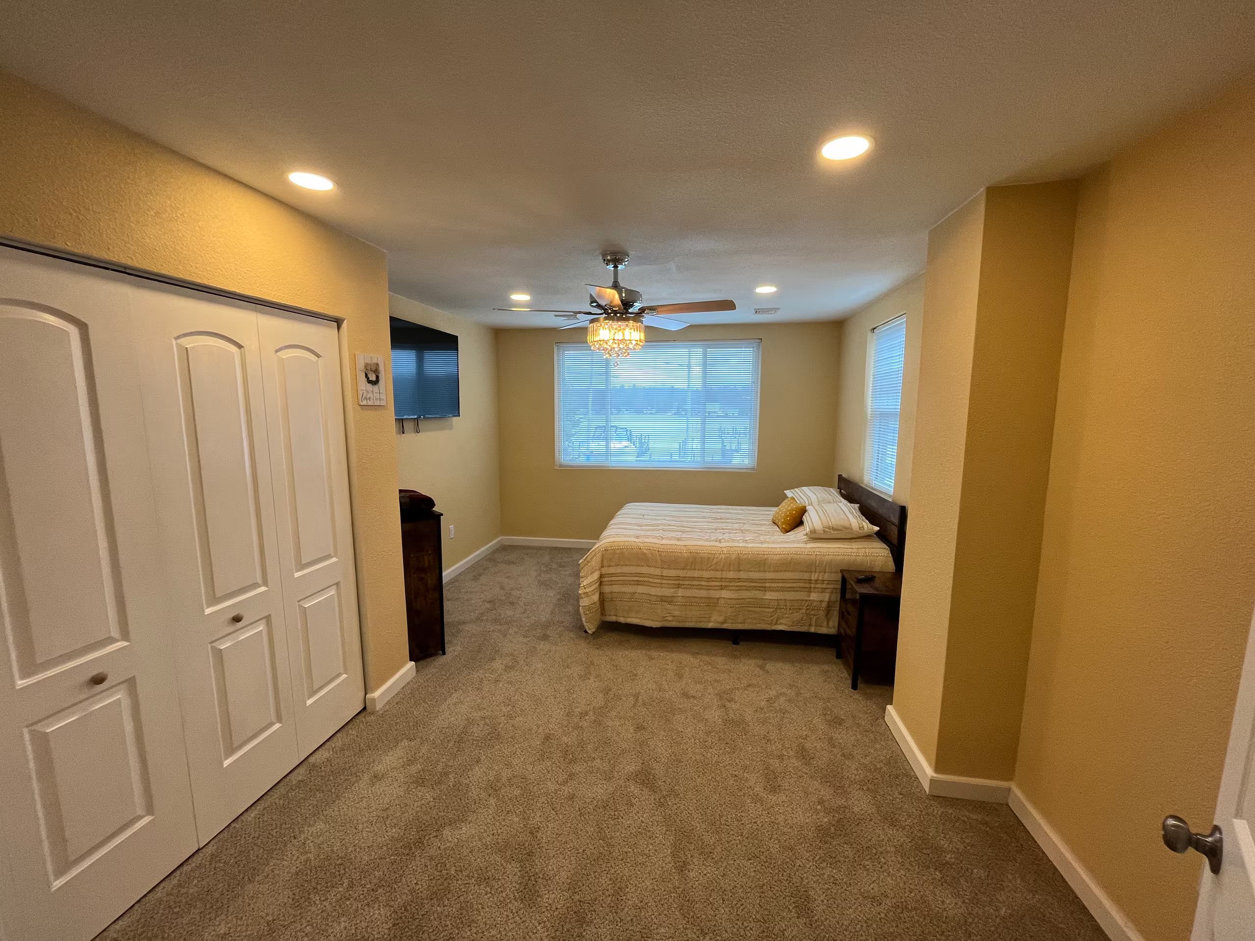 A bedroom with a bed, a ceiling fan, a window with blinds, and a door.