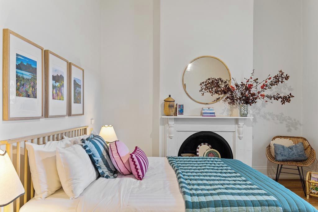 A bedroom with a bed, pillows, a bedside lamp, a fireplace, a mirror, and framed pictures on the wall.