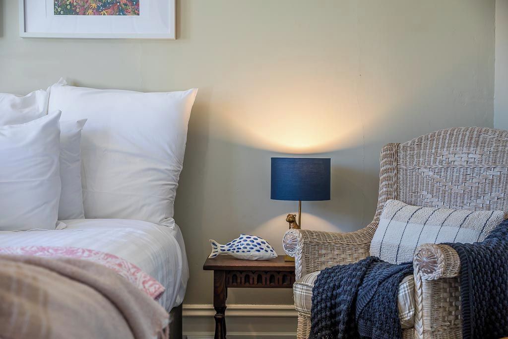 A hotel room with a bed, a chair, a nightstand, and a wall-mounted lamp.