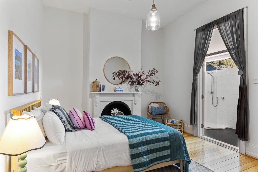 Une chambre à coucher comprenant un lit, une lampe de chevet, un miroir, une cheminée et donnant sur un espace douche.