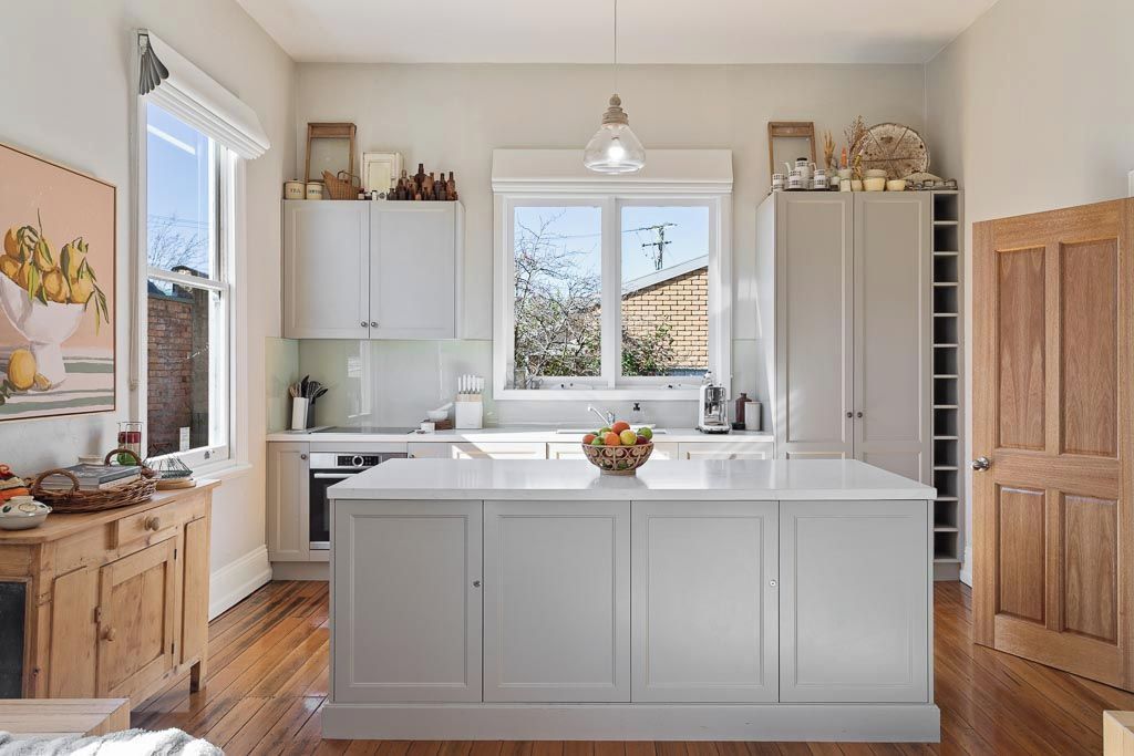 A modern kitchen with white cabinetry, a central island, and a large window providing natural light.