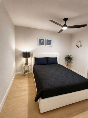Un dormitorio con una cama, un ventilador de techo, una lámpara de noche, dos obras de arte en la pared y un adorno mural.