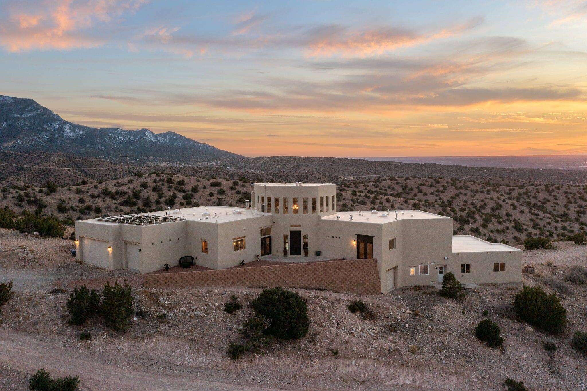 Un edificio moderno de varios pisos con techo plano, rodeado por un paisaje desértico y montañas al fondo.