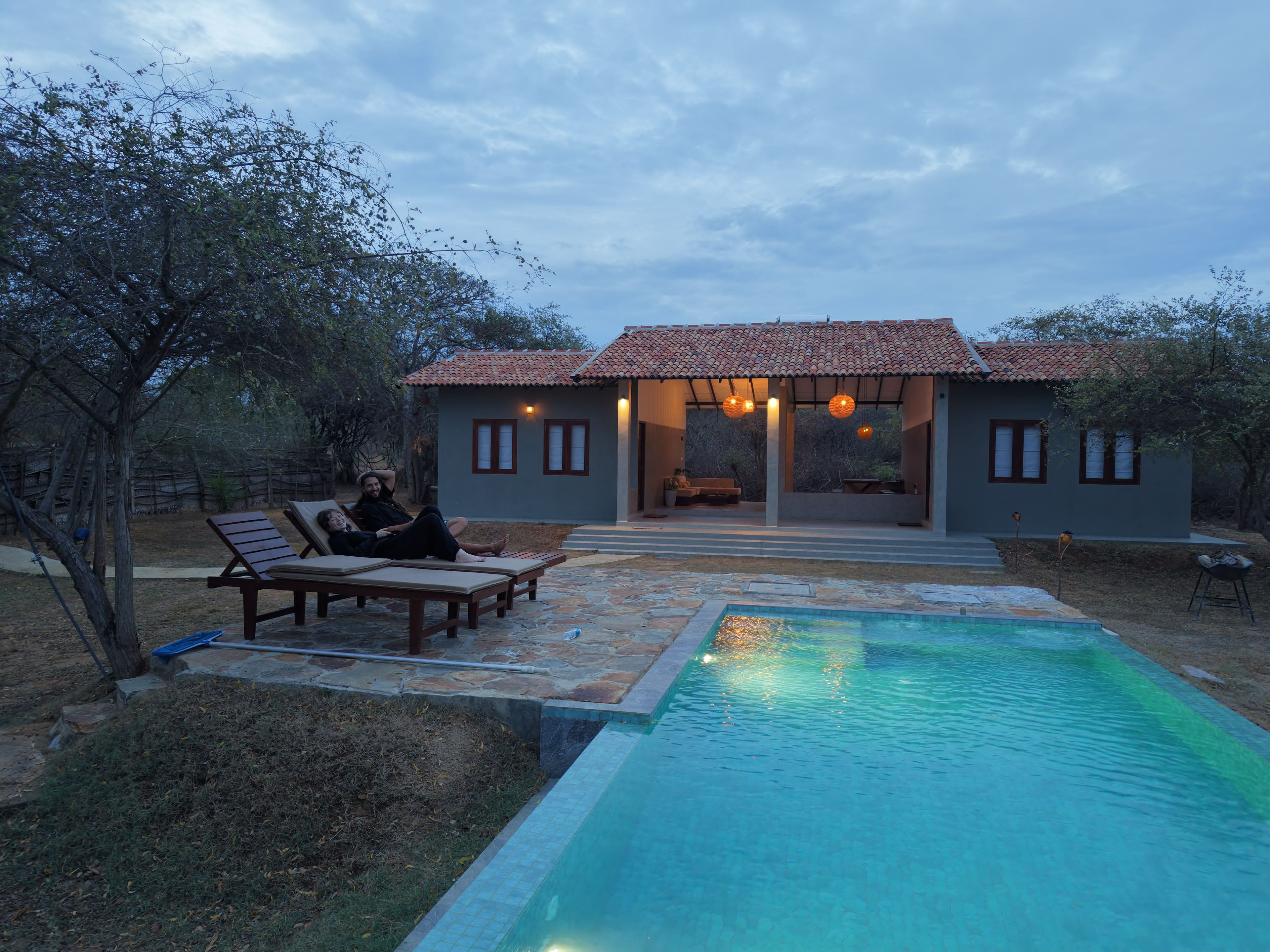 Área da piscina com espreguiçadeiras e uma casa ao fundo.