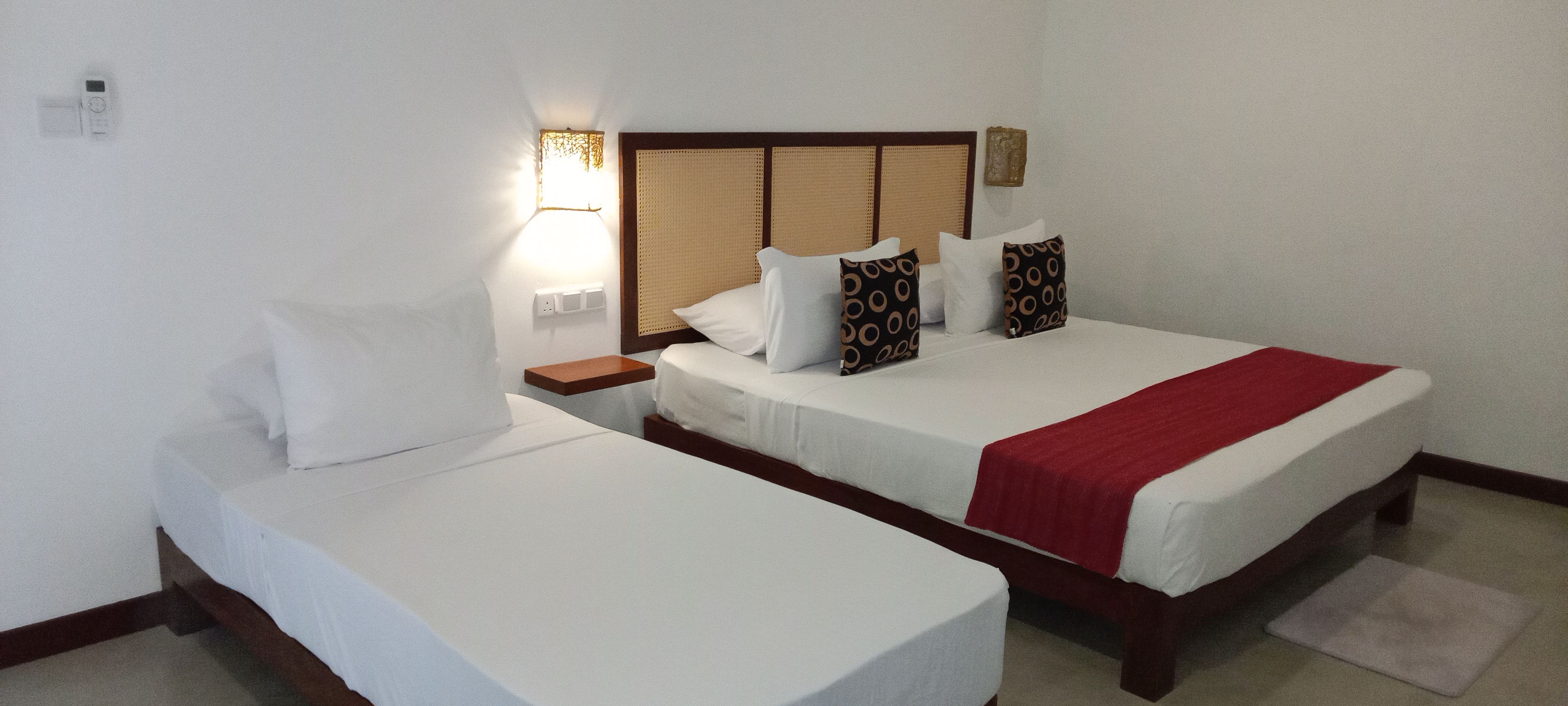 A hotel room with two single beds, a nightstand, a lamp, and a wall-mounted shelf.