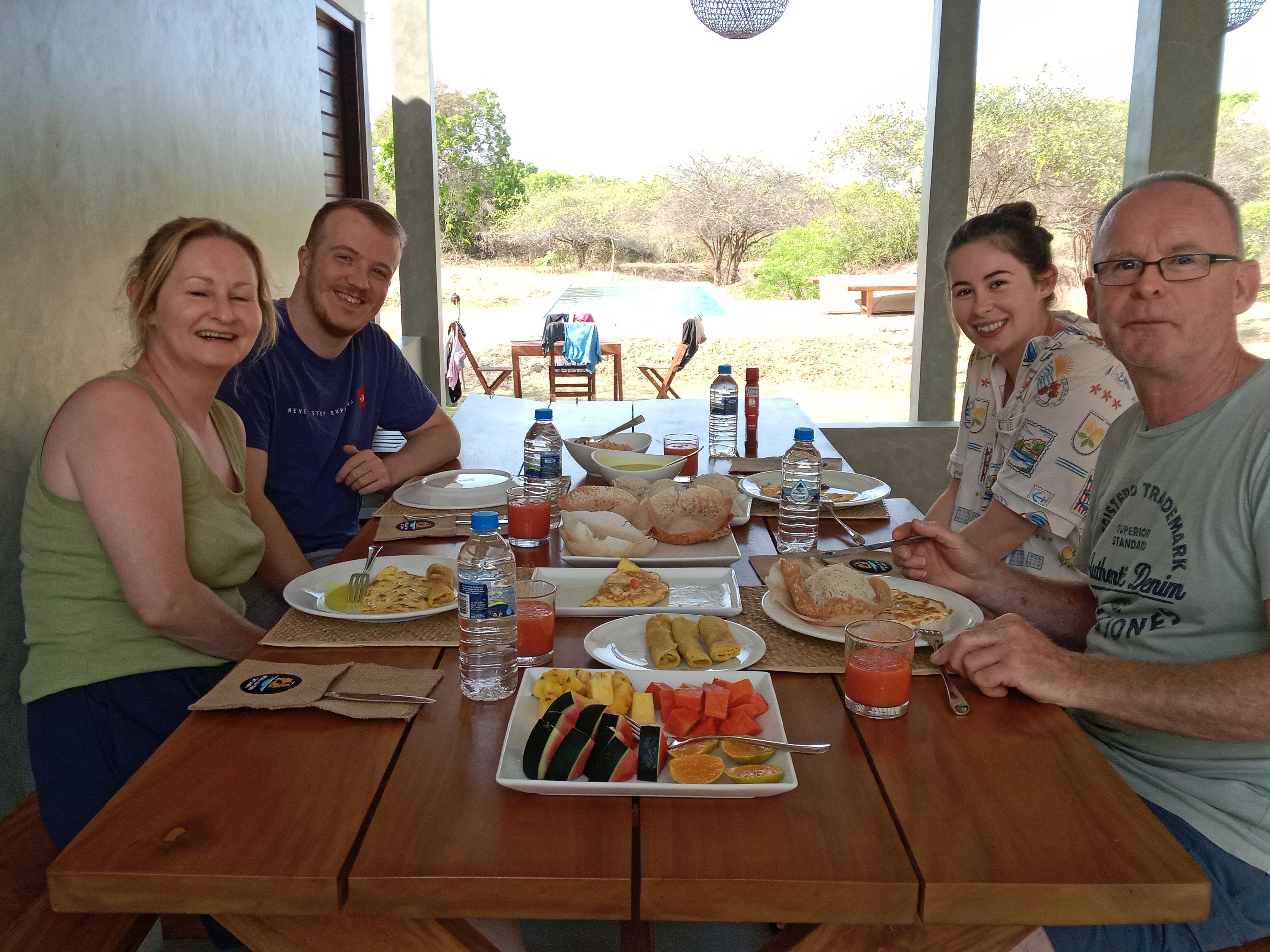 A group of people seated at a wooden table with various food items and drinks.