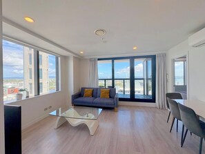 Een moderne woonkamer met een bank, een glazen salontafel en een eethoek met stoelen.
