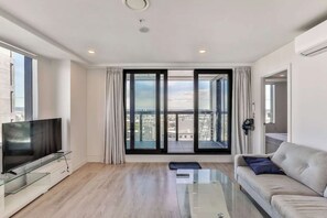 A modern living room with a flat-screen TV, a glass coffee table, a sofa, and large sliding glass doors offering a city view. - Stunning Seaview+Skytower View 2 Bedroom Apartment (Auckland central)