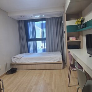 Una stanza arredata con un letto, una scrivania, una sedia, una televisione e una finestra con tende.