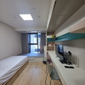 Una camera d'albergo con un letto, una scrivania con un computer, una televisione e una finestra con tende.