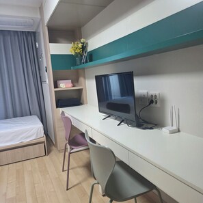 A hotel room with a bed, a desk with a computer, a chair, and a shelf with a vase of flowers. - [5 Min to Myeongdong] Twin Beds · Walk-in Closet · Separate Shower (Seoul)
