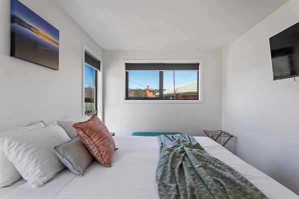 A bedroom with a bed, pillows, a blanket, a window, and a television on the wall. - Pioneer's Rest - two homes at Branxholm, near Derby (Branxholm)