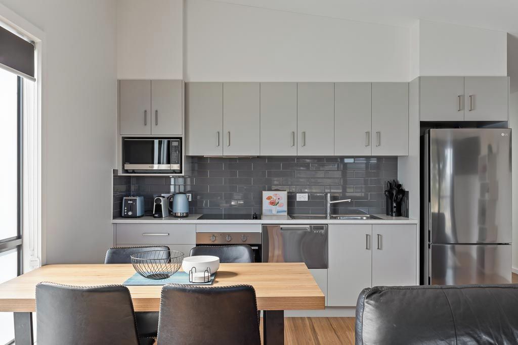 Een moderne keuken met grijze kastjes, roestvrijstalen apparatuur en een eetgedeelte met een houten tafel en stoelen.
