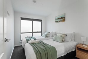 Ein Hotelzimmer mit zwei Betten, einem Fenster, einem Gemälde und einem Nachttisch mit Lampe.