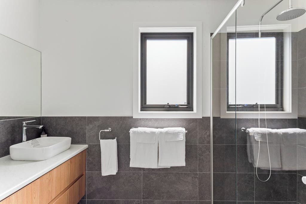 Een moderne badkamer met een grote spiegel, een witte wastafel, twee handdoekrekken en een douche.