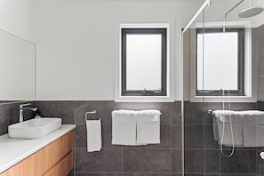 A modern bathroom with a large mirror, a white sink, two towel racks, and a shower area. - Pioneer's Rest - two homes at Branxholm, near Derby (Branxholm)