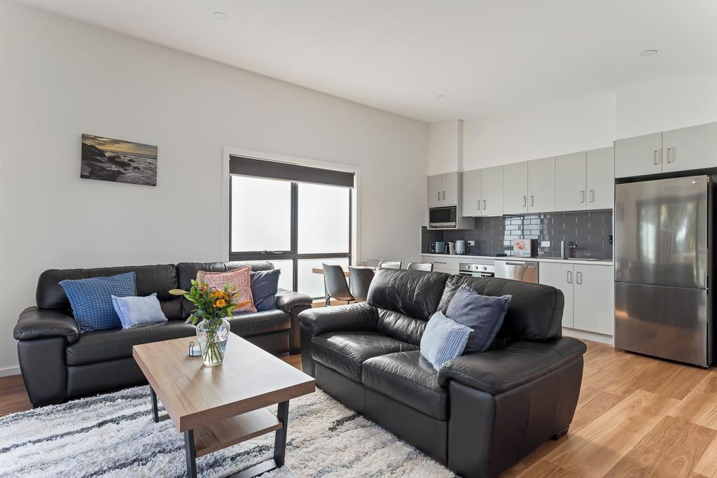A modern living room with a sofa, coffee table, and a kitchen area with cabinets and appliances.