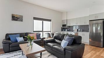 A modern living room with a sofa, coffee table, and a kitchen area with cabinets and appliances.