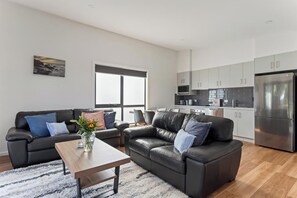 A modern living room with a sofa, coffee table, and a kitchen area with cabinets and appliances. - Pioneer's Rest - two homes at Branxholm, near Derby (Branxholm)